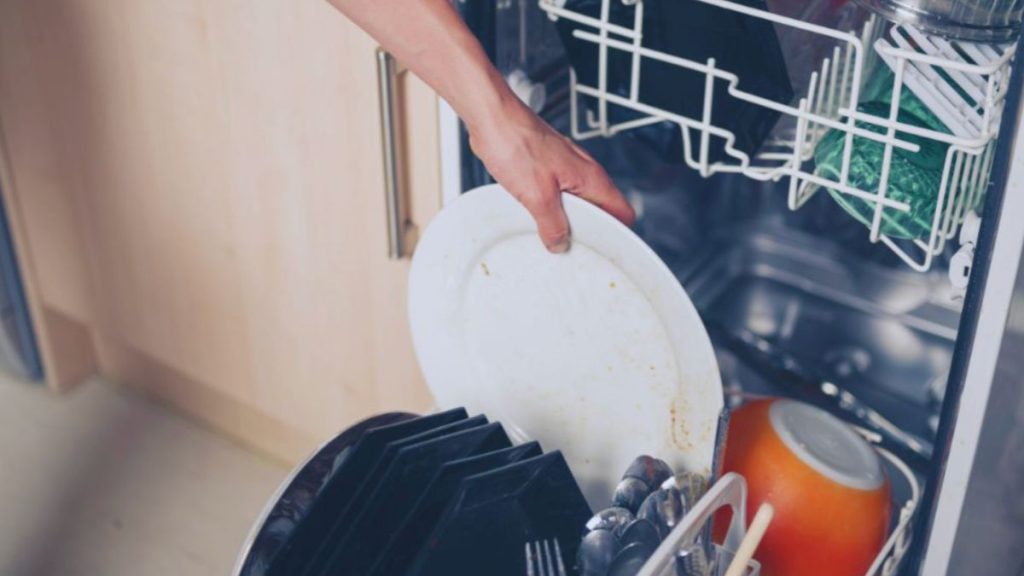 A person inserting a plate into a dishwasher, highlighting the functionality of this essential kitchen appliance.