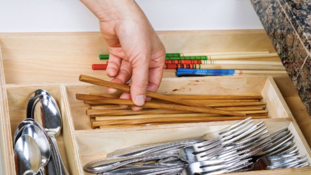 A person opens a drawer filled with organized utensils and spoons, showcasing effective kitchen storage solutions such as drawer dividers.
